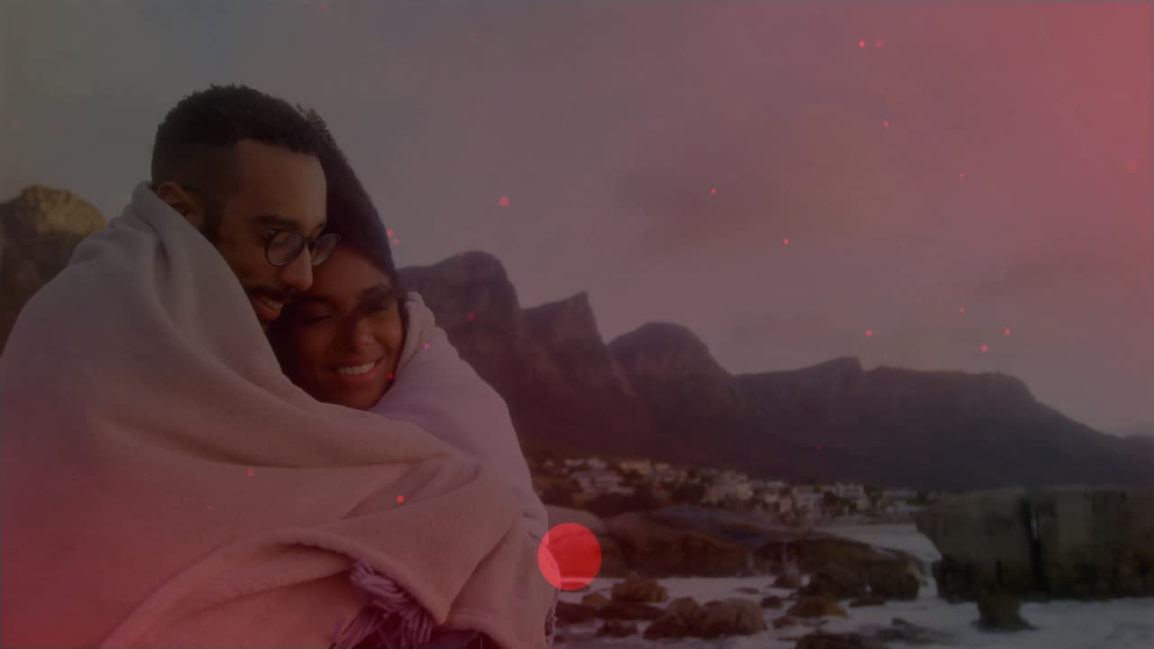 woman hugging partner under blanket on shoreline at sunset showing technology map and weather icons