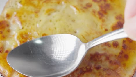 close up of a spoon spreading jam on a freshly cooked tempting pancake