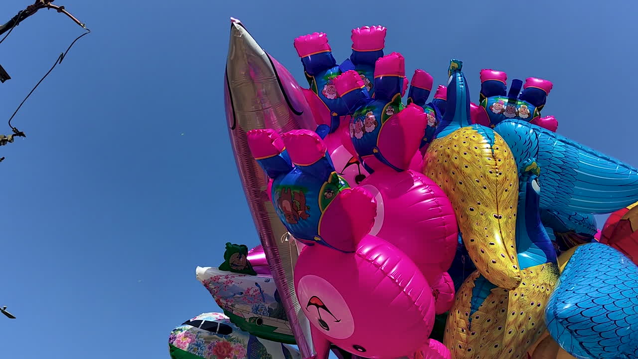 青空の下、露天商が販売する鮮やかな動物のビニール風船。祭りプロモーション、子供時代のテーマ、ストリートマーケットのビジュアル、カラフルなライフスタイルコンテンツに最適です。