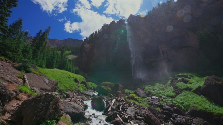 Paesaggio estivo del Colorado: Cascate Bridal Veil nel Telluride Box Canyon, panoramica lenta verso il basso lungo la parete rocciosa. Centrale idroelettrica, Passo Black Bear. Cielo azzurro e soleggiato, nuvole, nebbia, spruzzi e scenario.