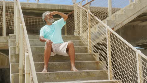 front view of active senior african american man with shielding eye sitting on stair at promenade 4k