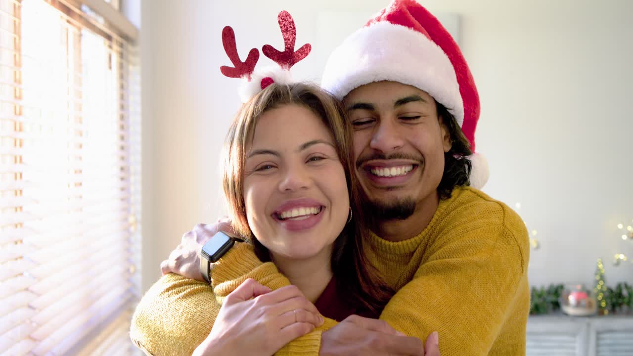 Pareja romántica abrazándose junto a una ventana después de que un hombre con gorro de Papá Noel se acerque a una mujer con astas para celebrar la alegría festiva