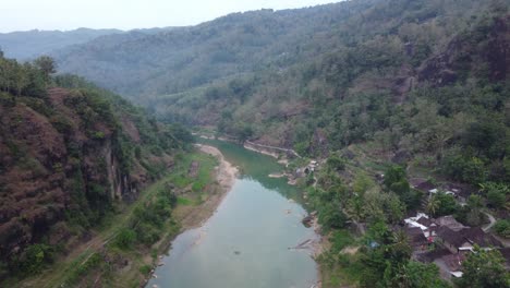 Beautiful-aerial-view-of-a-river-in-the-middle-of-the-mountains-in-the-morning-with-village-housing-on-the-river-bank