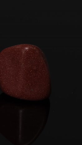 una piedra de oro roja gira sobre una superficie reflectante.