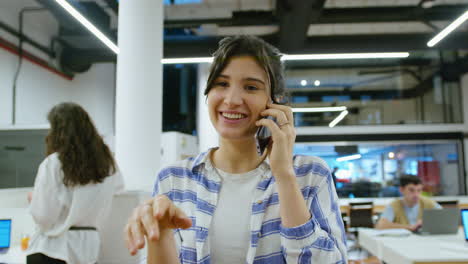 Young Cheerful Businesswoman Walking Through Office and Speaking on Phone