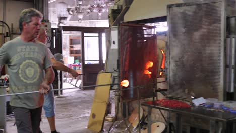 two glass artist demonstrate how to make traditional glass using heated oven in a glass factory