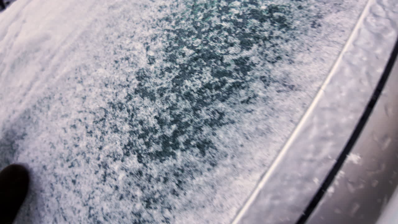 Man with brown leather gloves uncovering the car front window from frozen snow in winter