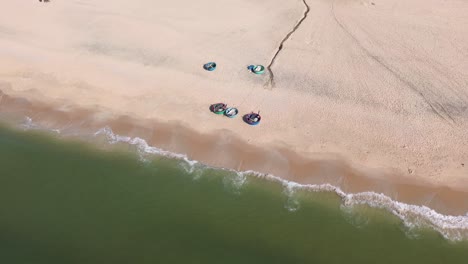 drone flies left to right in a half-circle above mui ne beach, filming colorful swimming buckets parked on white sand, revealing the shore, beach, and sparkling turquoise sea.