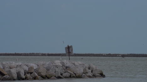 stationary-shot-of-break-wall-on-Lake-Erie-with-seagulls-flying-around-with-blue-skies