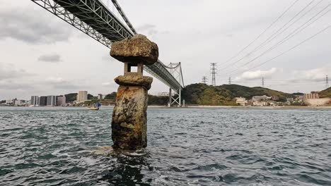 old japanese rock lantern halfly submerged in water in front of kanmon bridge and the kanmon strait in between the japanese island honshu and kyushu