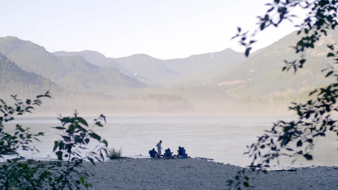Friends gathering on a lakeside beach, sitting on lawn chairs and drinking beer