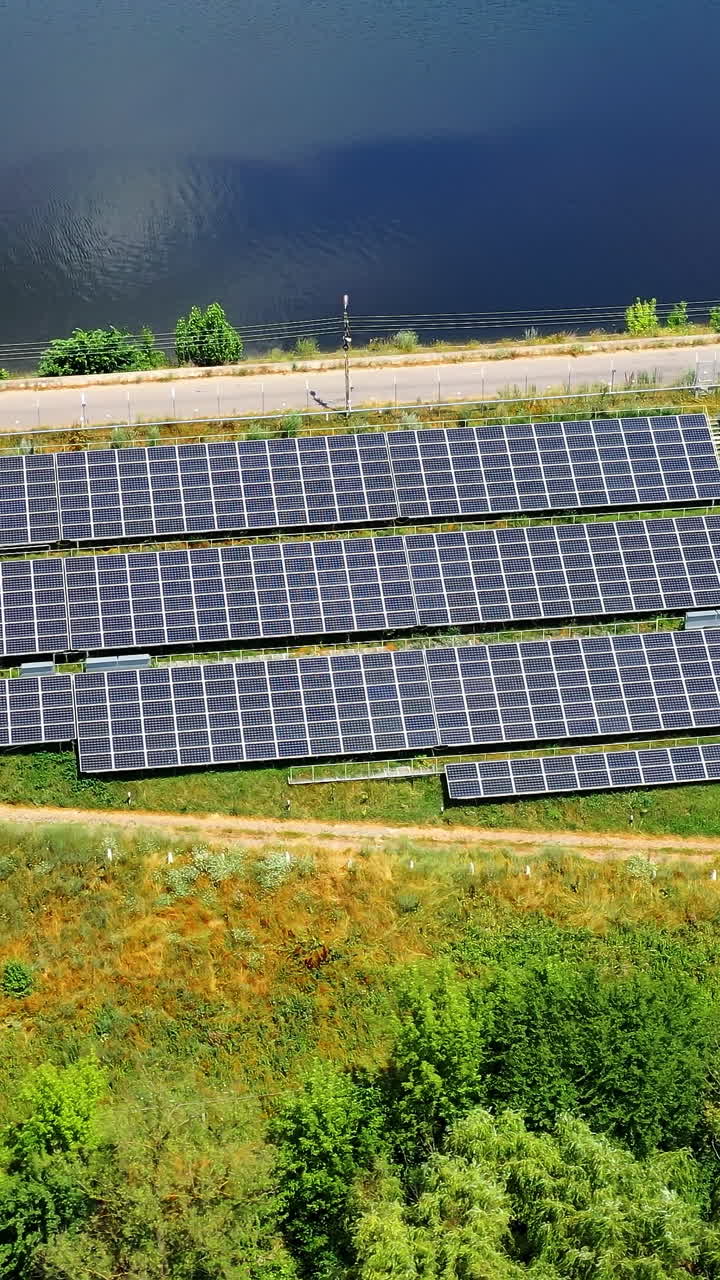 Flight over long solar panels on field. Photovoltaic solar cells near the road at bright sunny day. Alternative green energy. Aerial view. Vertical video
