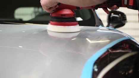 the car being waxed by a hand tool spinning to polish the grey reflective body