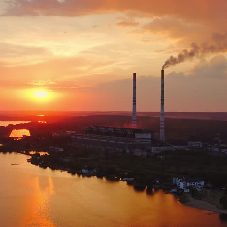 silhouette of a chemical plant near the river. industrial factory releases smoke at beautiful sunset time. dangerous manufacturing among nature. aerial view.