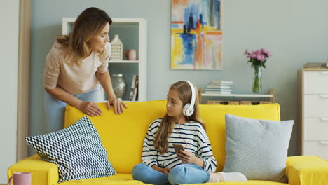 teenage girl with headphones listening to music sitting on yellow sofa while her mother speaks loud to her 1