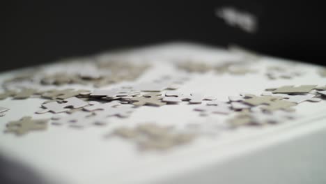 slow motion: close up of white and gray puzzle pieces falling on a white surface on a pile of pieces with a dark background. shot in 4k with shallow depth of field. smooth pan movement