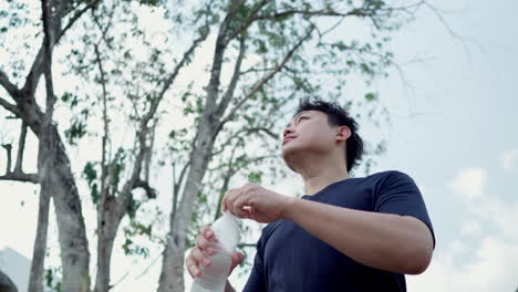 man drinking water from a plastic bottle water after workout in forest