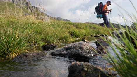 excursionista masculino caminando sobre un pequeño arroyo con piedras durante un día soleado en las dolomitas de lagorai, italia