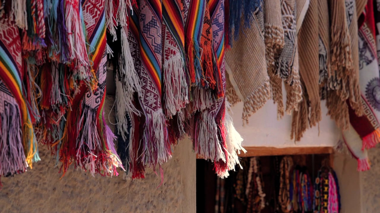 Ripresa ravvicinata al rallentatore di coperte tradizionali andine tessute e nappe colorate che ondeggiano dolcemente nella brezza in un mercato a Cusco, Valle Sacra, Perù