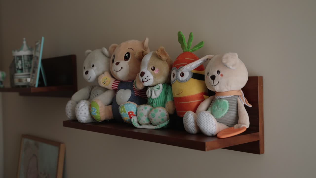 Five colorful stuffed toys sit neatly on a wall mounted wooden shelf in a child’s room