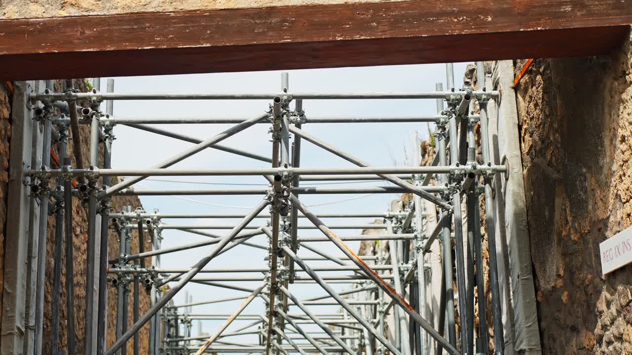 Close-up view through a Pompeii doorway into dense restoration scaffolding, highlighting ongoing conservation work around ancient Roman stone walls and structural remains