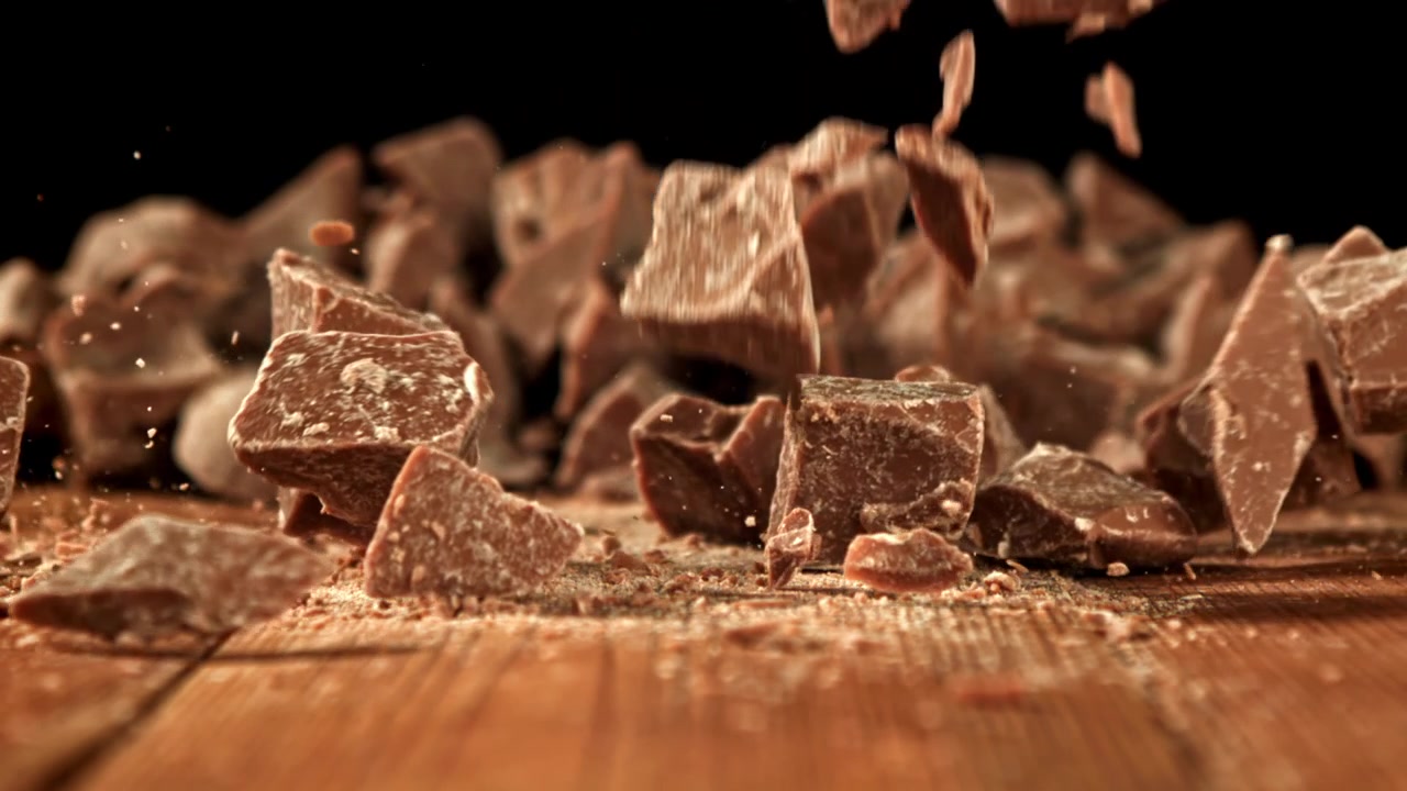 Pezzi di cioccolato che cadono al rallentatore su un tavolo di legno