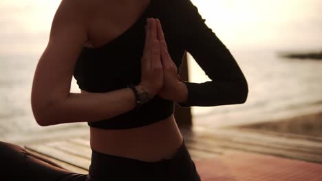 Woman-Practicing-Yoga-And-Stretching-Spine-And-Hands-Sitting-On-Mat-On-Sea-Pier-Joins-Hands-Behind-Her-Back