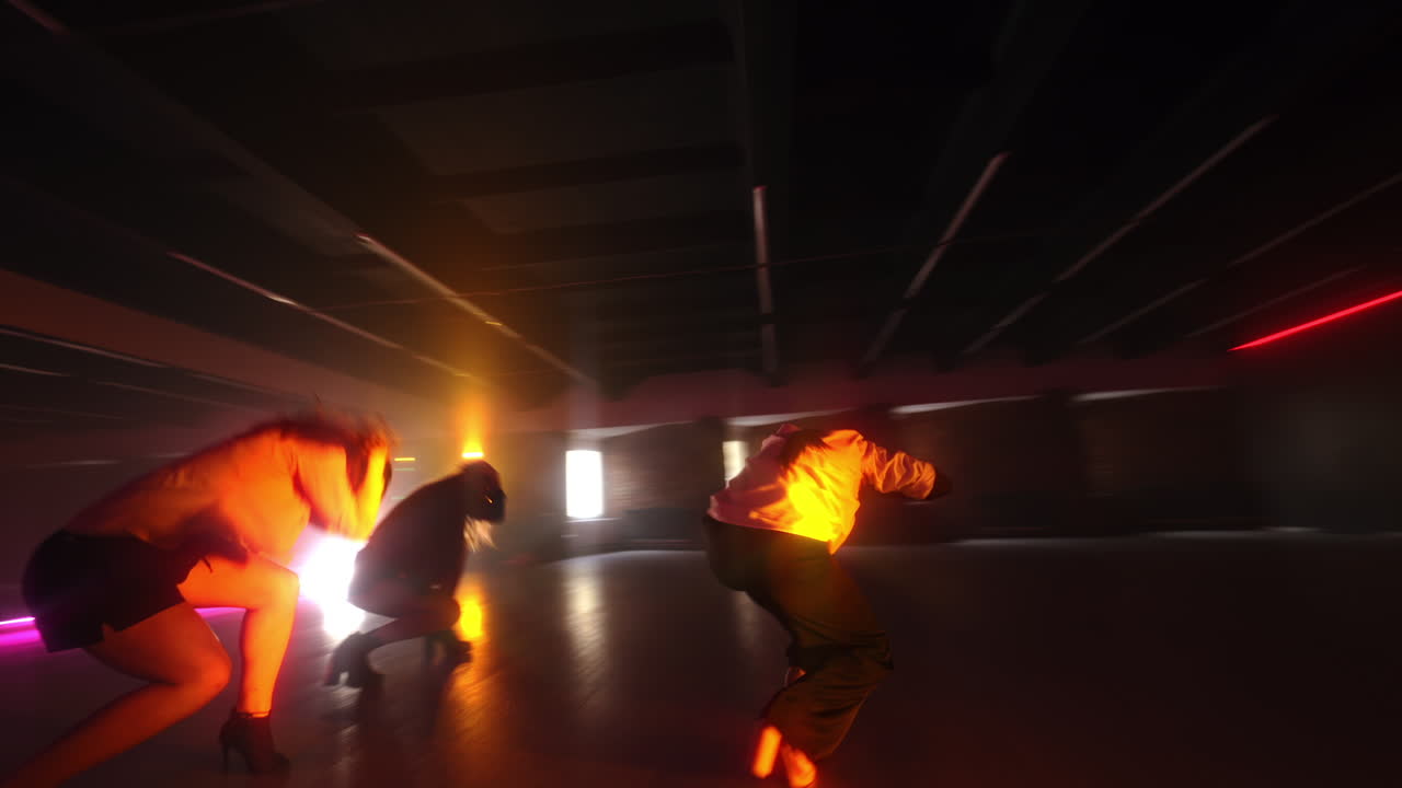Dancing trio performing in the studio with pink light. Girls dance actively on high hills. Low angle view.