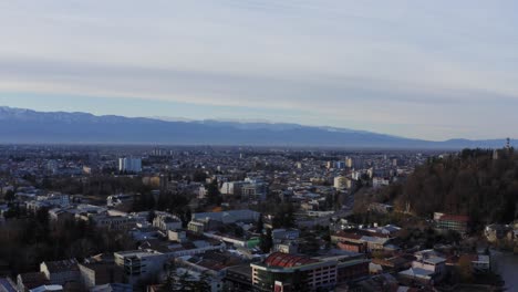 Aerial-flying-over-Kutaisi-city-with-snowy-mountains-and-river