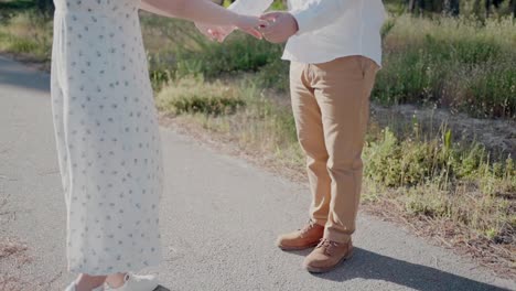 a couple holding hands, standing on a sunlit path, showcasing their footwear and lower outfits