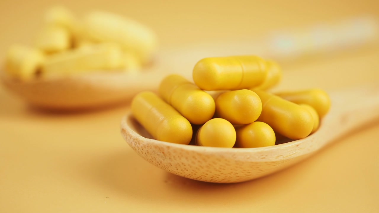 Yellow Capsules in a Wooden Spoon on a Yellow Background