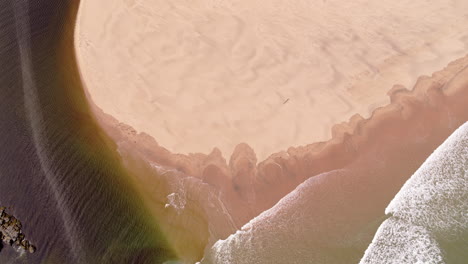 Aerial-shot-looking-down-at-waves-breaking-on-the-beach-on-a-sunny-day