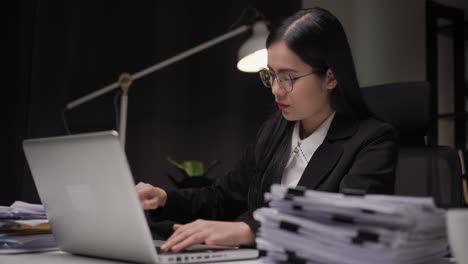 young asian business woman working at late night. she was very busy checking paperwork and had to send the work before the deadline, feeling stressed. sitting in the dark office at night.