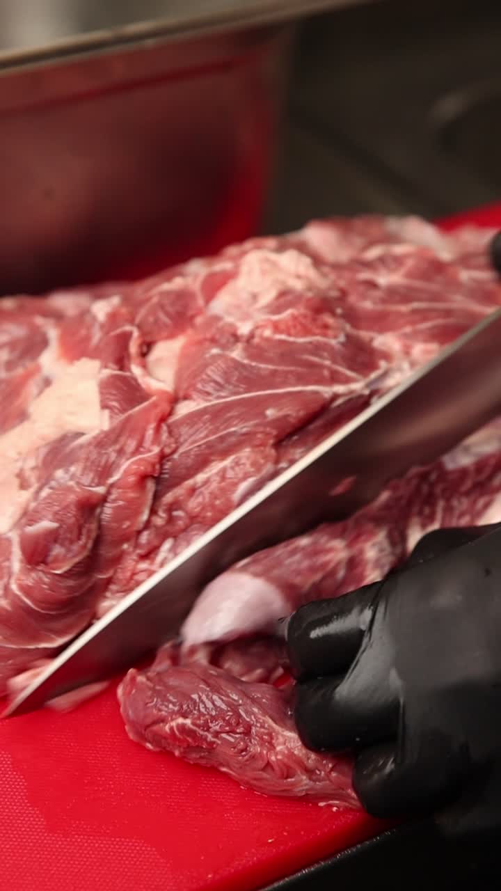 Chef che taglia carne cruda con un coltello su un tagliere rosso