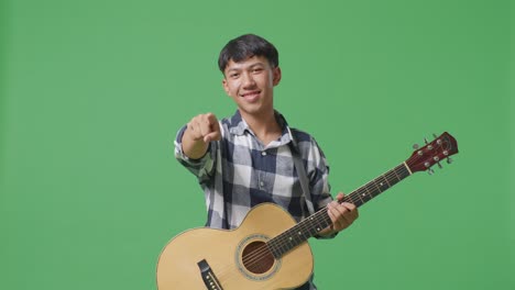 asian teenager with guitar making honest gesture and smiling on green screen background