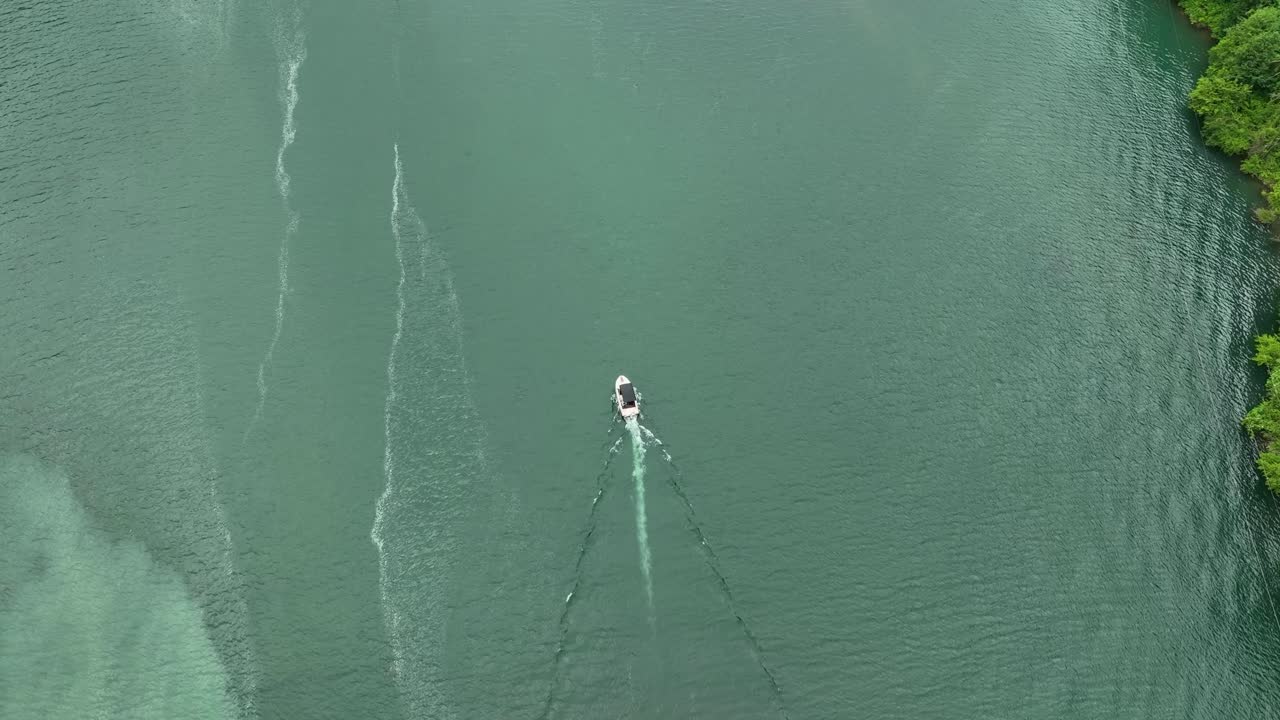 A peaceful aerial view of a green-tinted lake with small boats drifting across the still water, surrounded by lush forest edges
