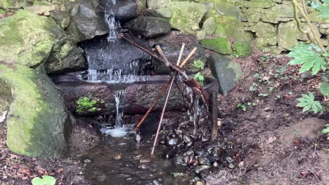 a shishi-odoshi in a japanese garden with the sound of a bamboo rocker arm hitting a rock showing water flow