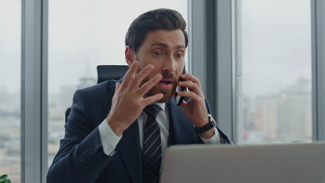 Annoyed-director-arguing-phone-call-sitting-at-office-desk-closeup.-Man-shouting