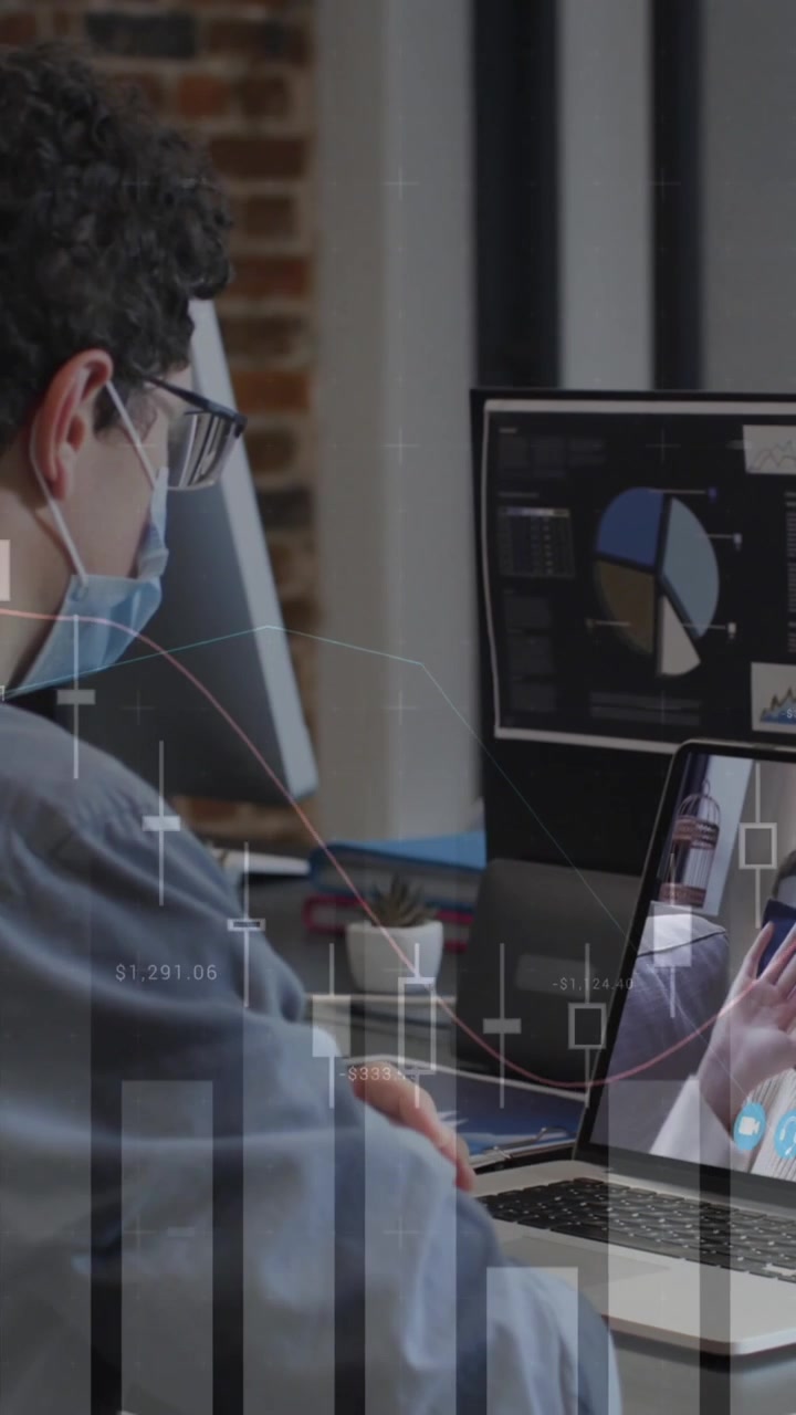 Animation of financial graphs over caucasian man in face mask having video call in office