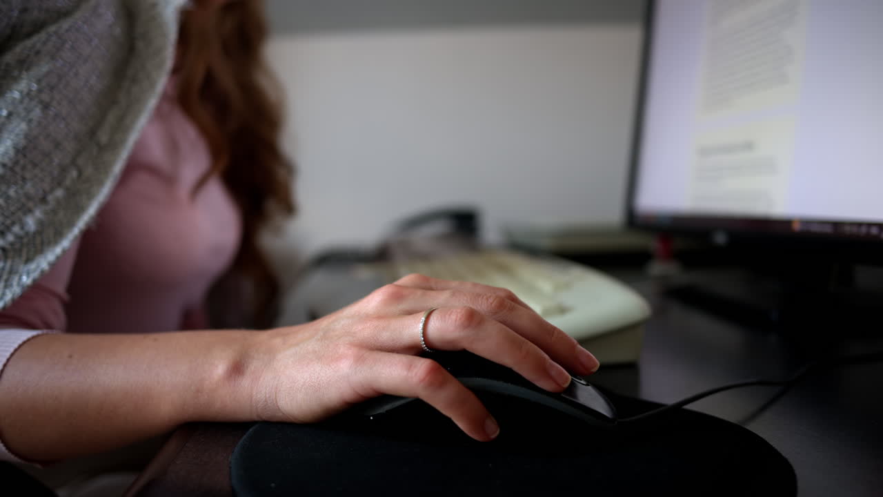 Woman working on a computer at the office, hand on black mouse