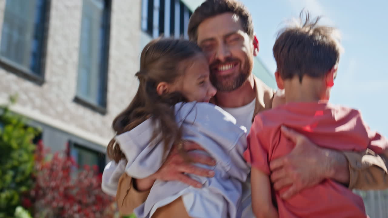 Relaxed father strolling sunshine square. Children running to dad embracing