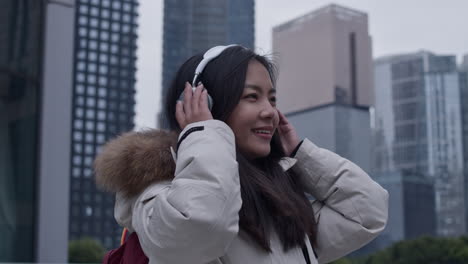 estudiante asiática feliz escucha música en auriculares inalámbricos afuera en la ciudad de guangzhou