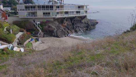 rising through the grass to reveal a small beach next to a cliff side apartment, in laguna beach, california