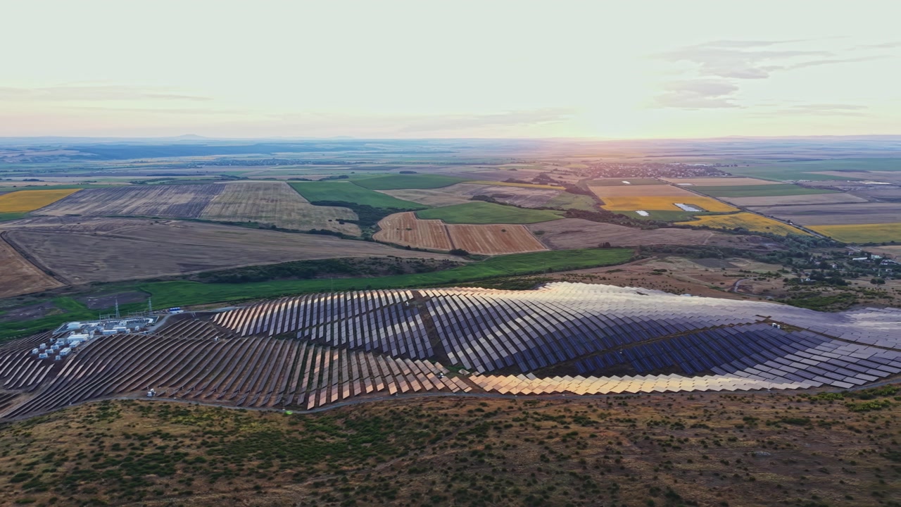 Solcellepark i et landområde ved solnedgang med udsigt til marker og bjerge i det fjerne