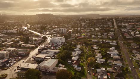 auckland city with cars on street during golden sunset. aerial wide shot. houses and homes. cloudy sky in summer. suburb residential area in new zealand.