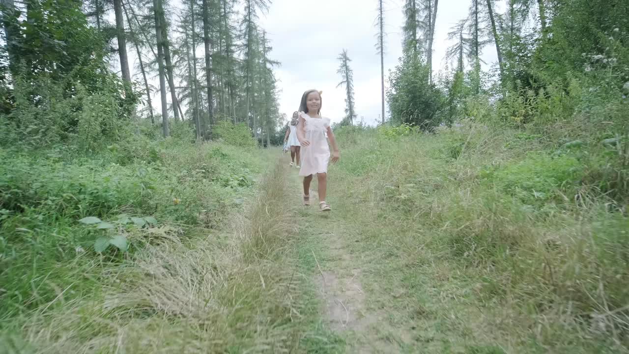 옷을 입은 임신부와 어린 딸이 잔디 인 공원을 가로질러 손을 잡고 걸어가는 장면은 나무로 둘러싸인 자연 속에서 가족의 유대감의 평온한 순간을 포착합니다.