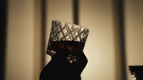 a hand swirling a glass of bourbon whiskey back lit