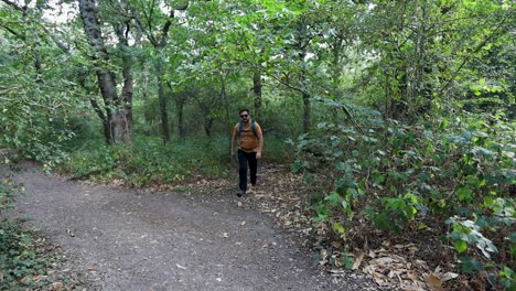 Slow-motion-of-young-man-with-a-backpack-and-sunglasses-comes-out-of-the-woods