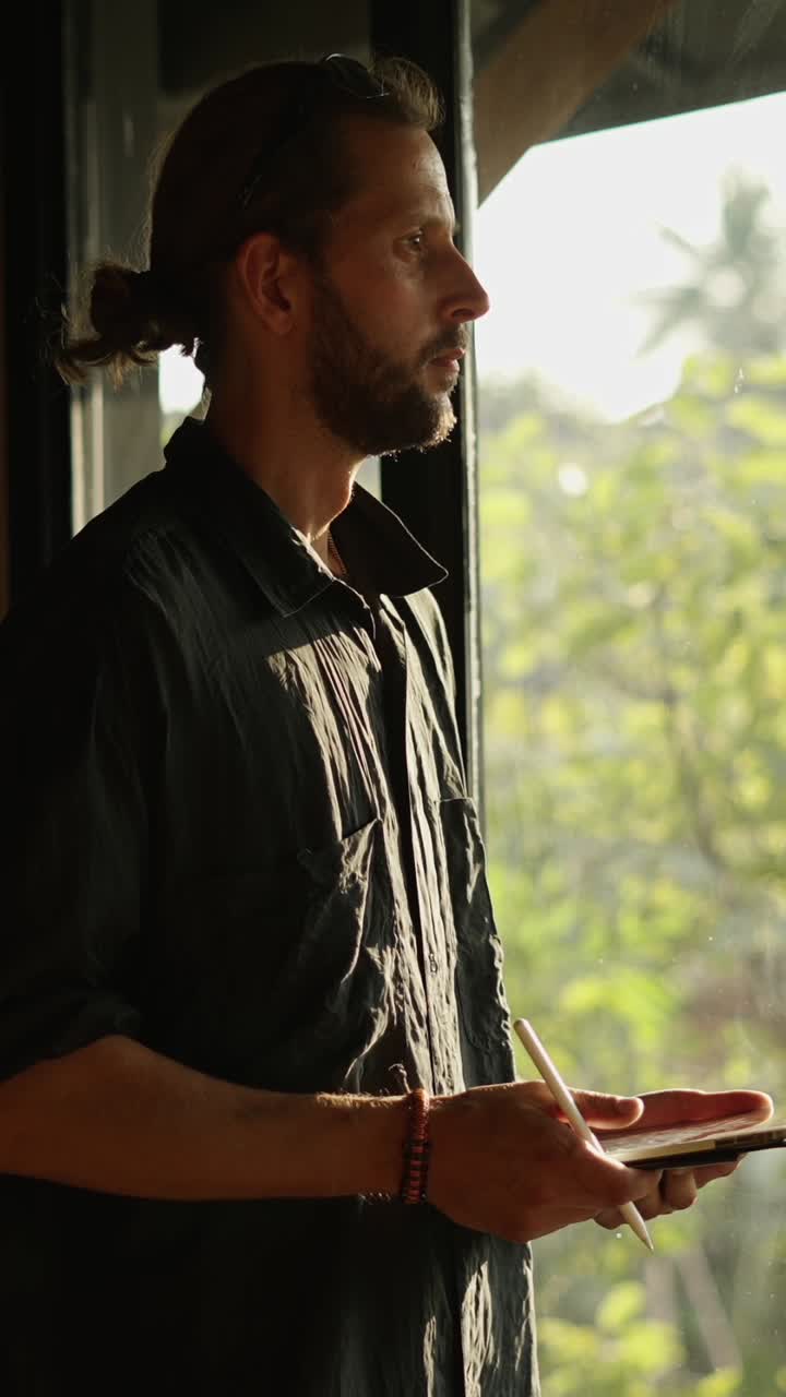 Man drawing on tablet by window