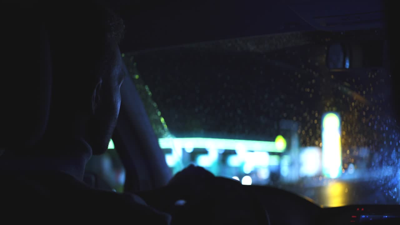 The young man drives the car through the night rainy highway